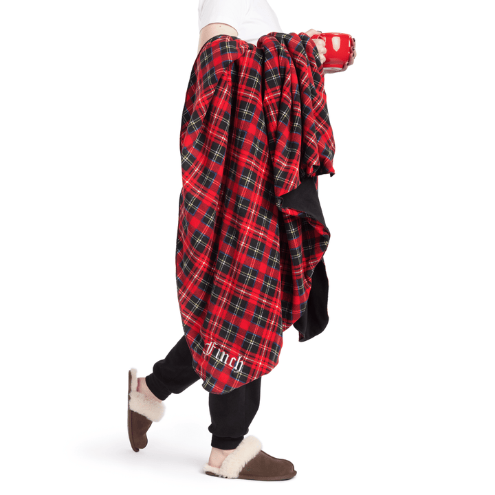 A person wears black joggers and carries a red plaid blanket in front of a white background