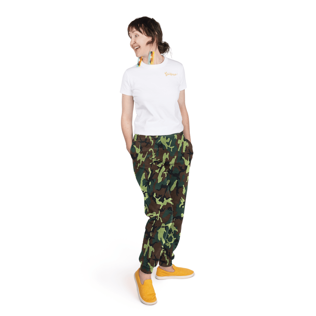 A woman stands wearing a white t shirt and camouflage fleece joggers in front of a white background