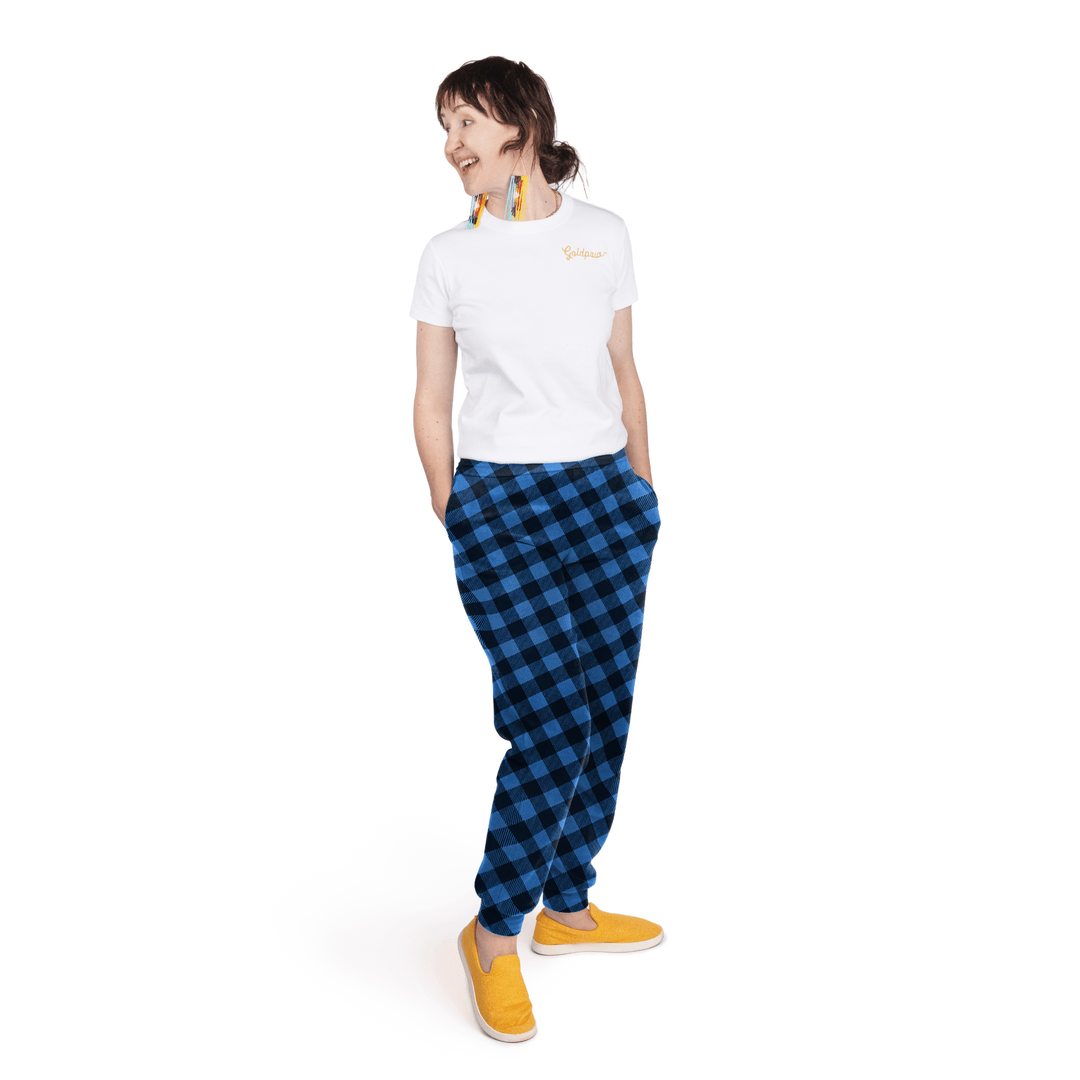 A woman stands wearing a white t shirt and cobalt and black buffalo check fleece joggers in front of a white background