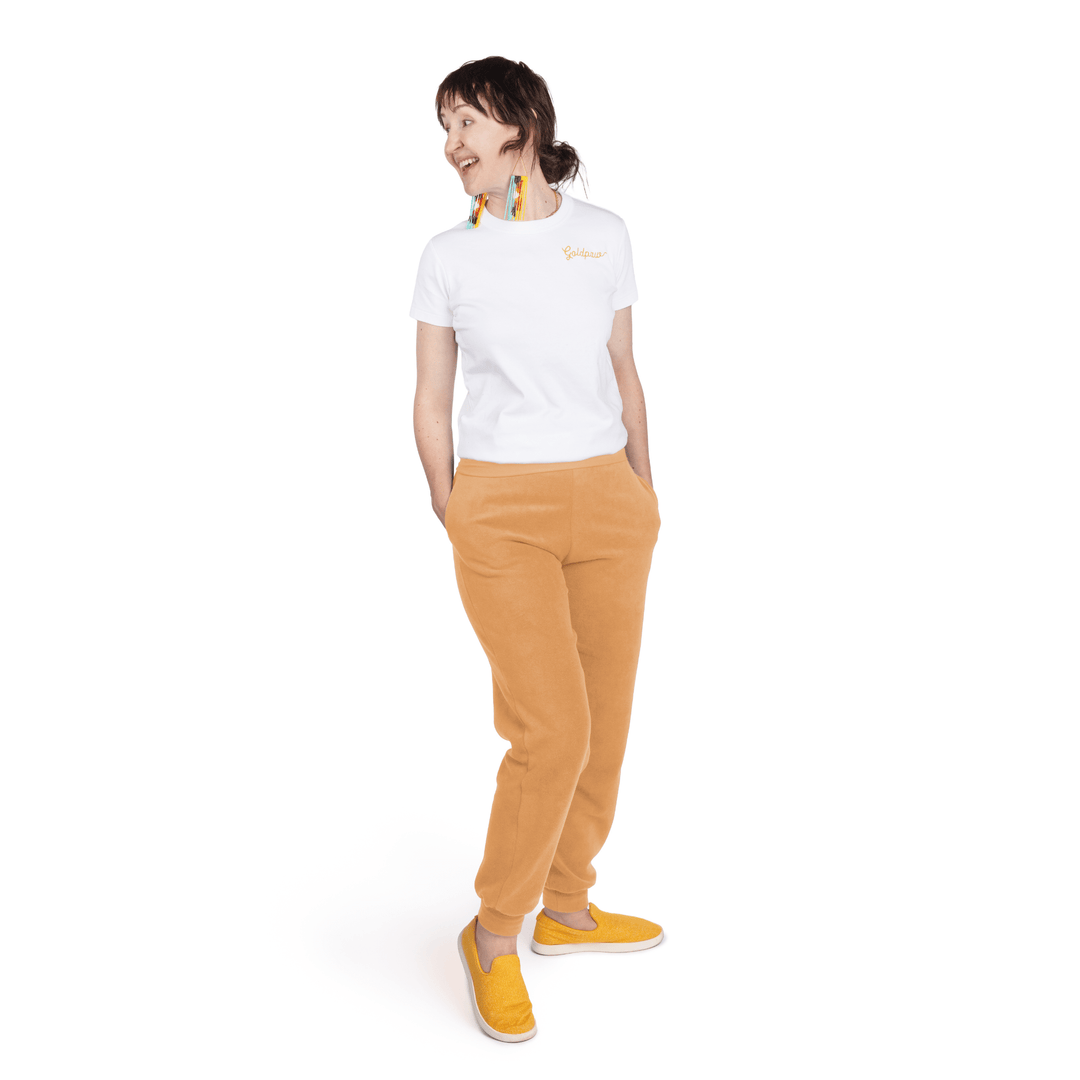 A woman stands wearing a white t shirt and cheddar orange fleece joggers in front of a white background