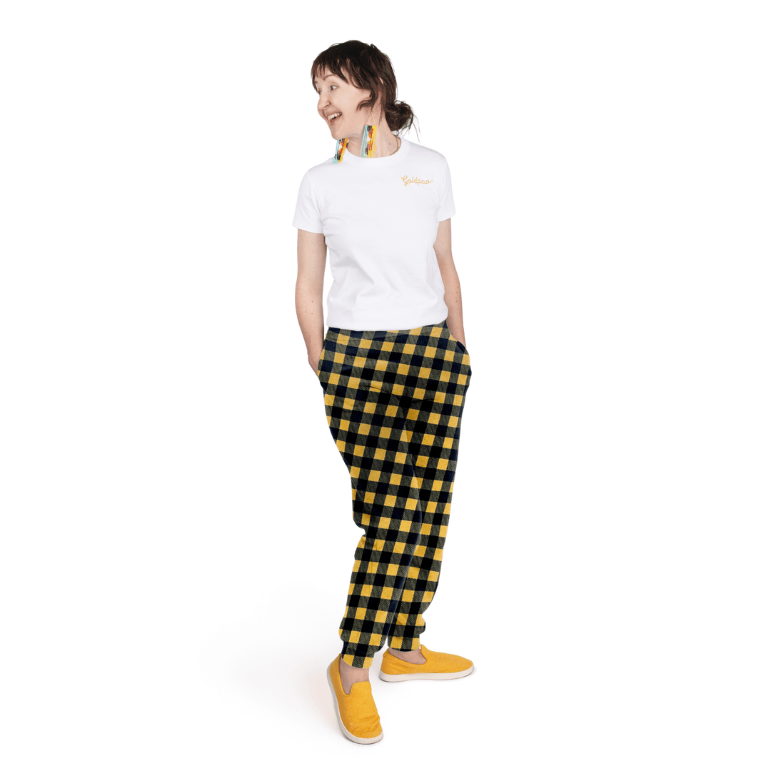 A woman stands wearing a white t shirt and gold and black buffalo check fleece joggers in front of a white background