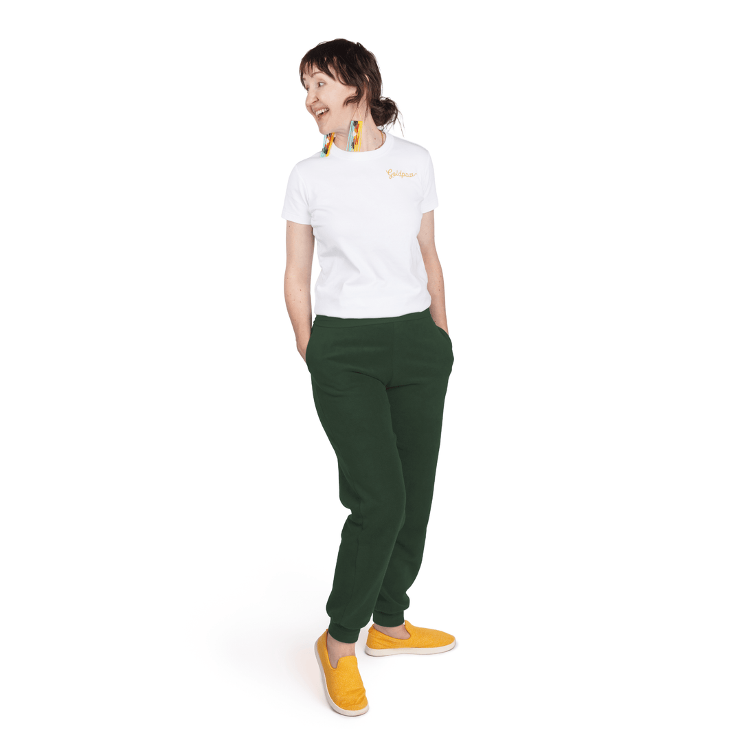 A woman stands wearing a white t shirt and hunter green fleece joggers in front of a white background