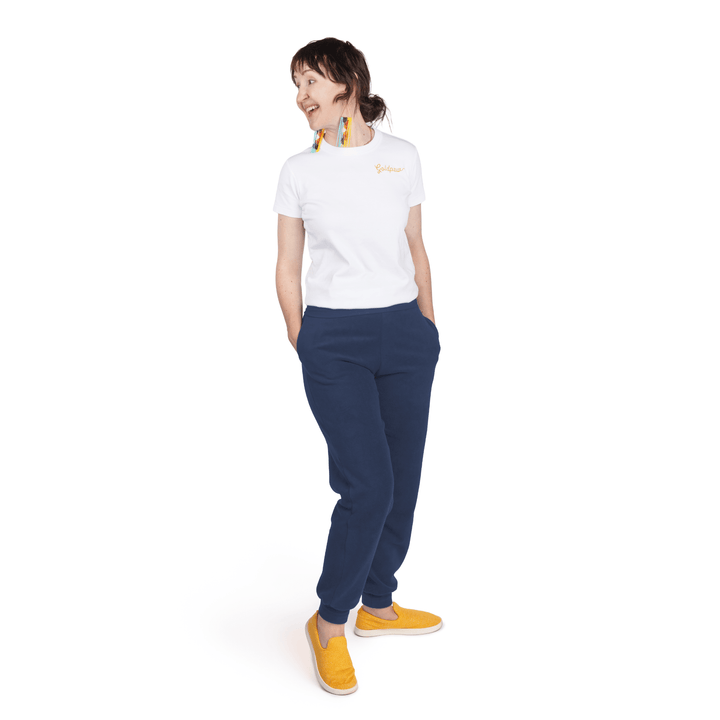 A woman stands wearing a white t shirt and navy fleece joggers in front of a white background