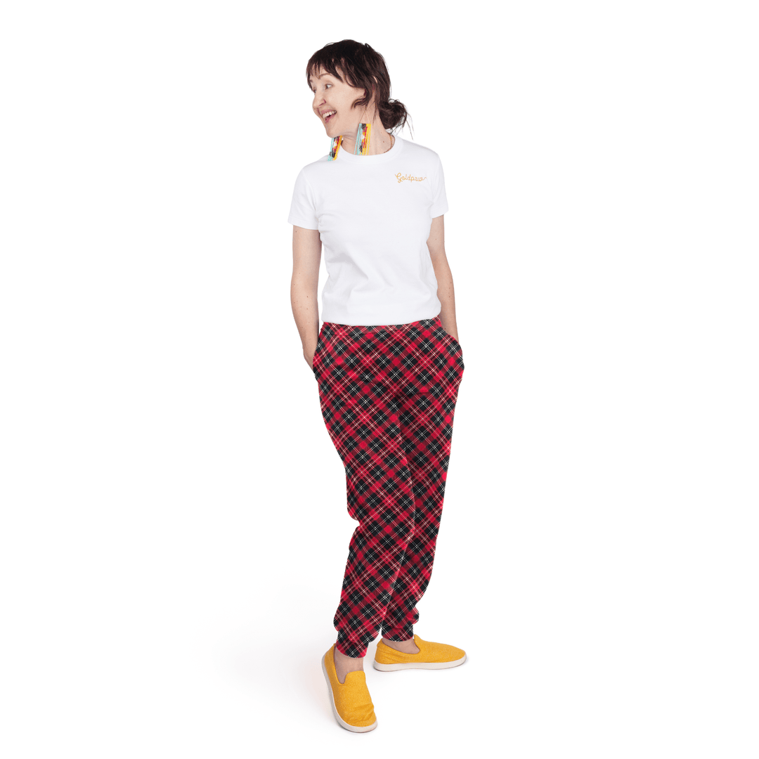 A woman stands wearing a white t shirt and red plaid fleece joggers in front of a white background