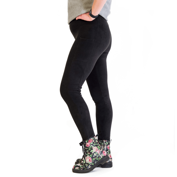 A woman stands wearing a grey shirt and black fleece leggings in front of a white background