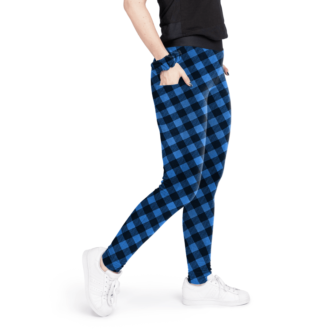 A woman stands wearing a black t shirt and cobalt and black buffalo check fleece leggings with a matching scrunchie on their wrist in front of a white background