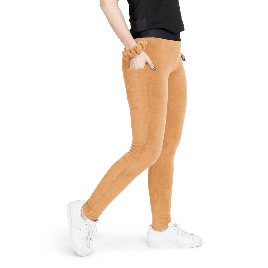 A woman stands wearing a black t shirt and chipmunk tan fleece leggings with a chipmunk tan scrunchie on their wrist in front of a white background