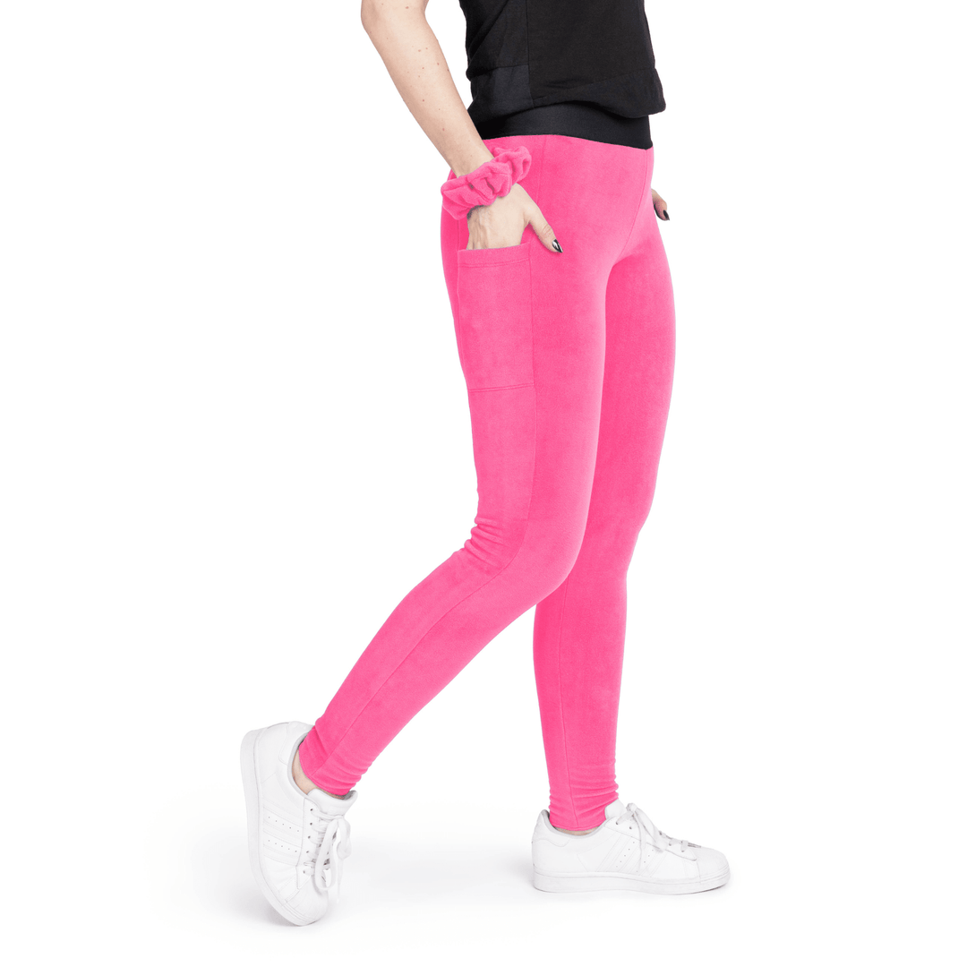 A woman stands wearing a black t shirt and hot pink fleece leggings with a hot pink scrunchie on their wrist in front of a white background