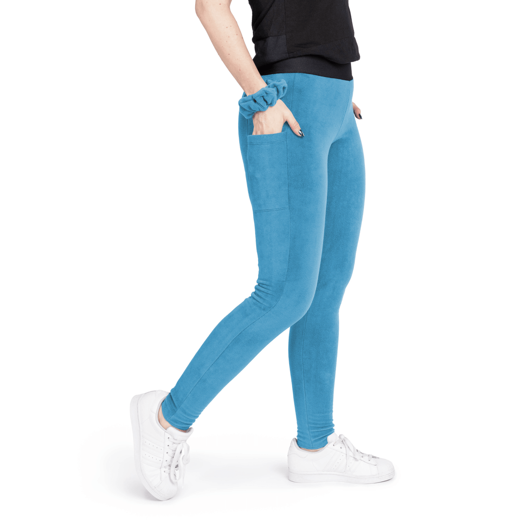 A woman stands wearing a black t shirt and marine blue fleece leggings with a marine blue scrunchie on their wrist in front of a white background