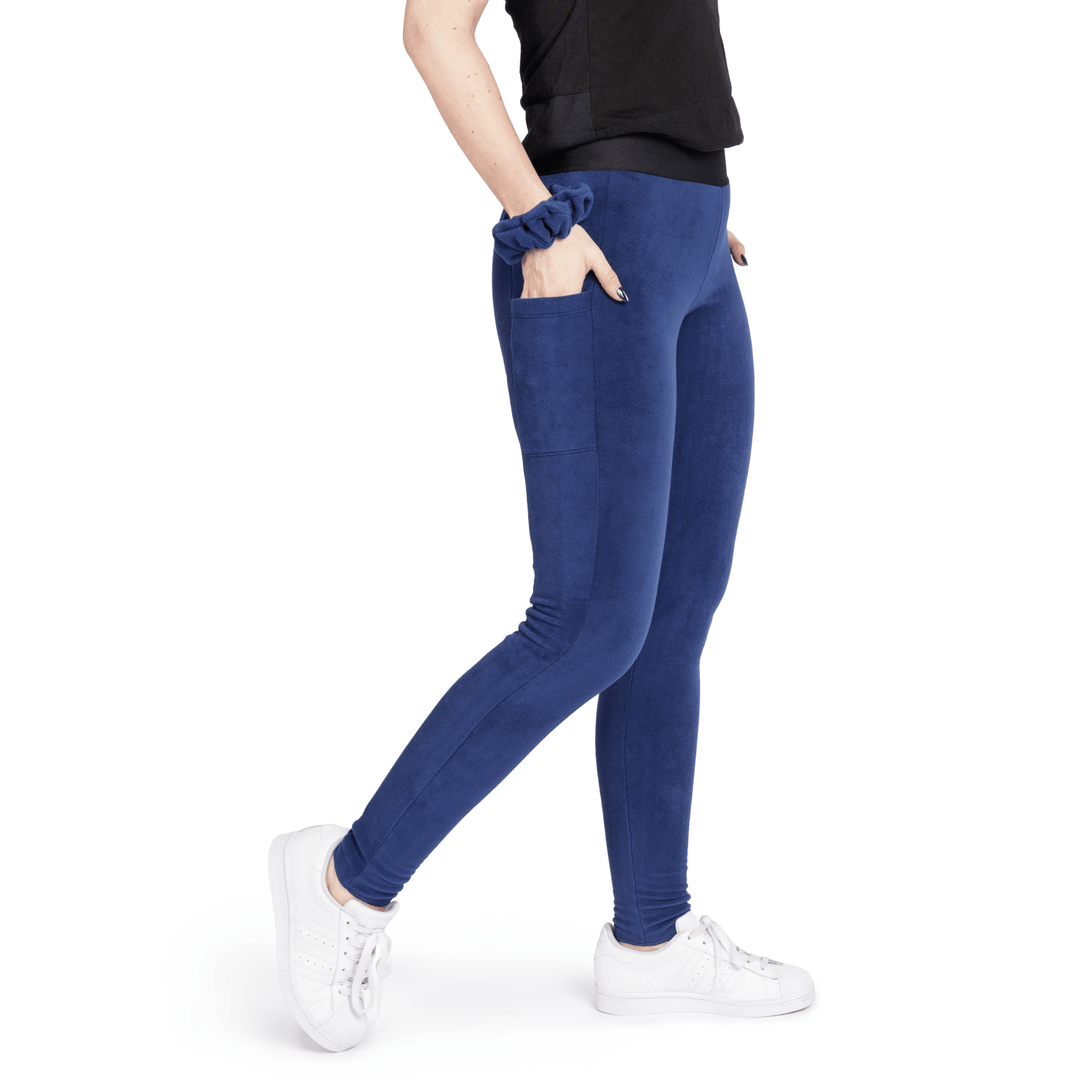 A woman stands wearing a black t shirt and navy fleece leggings with a navy scrunchie on their wrist in front of a white background
