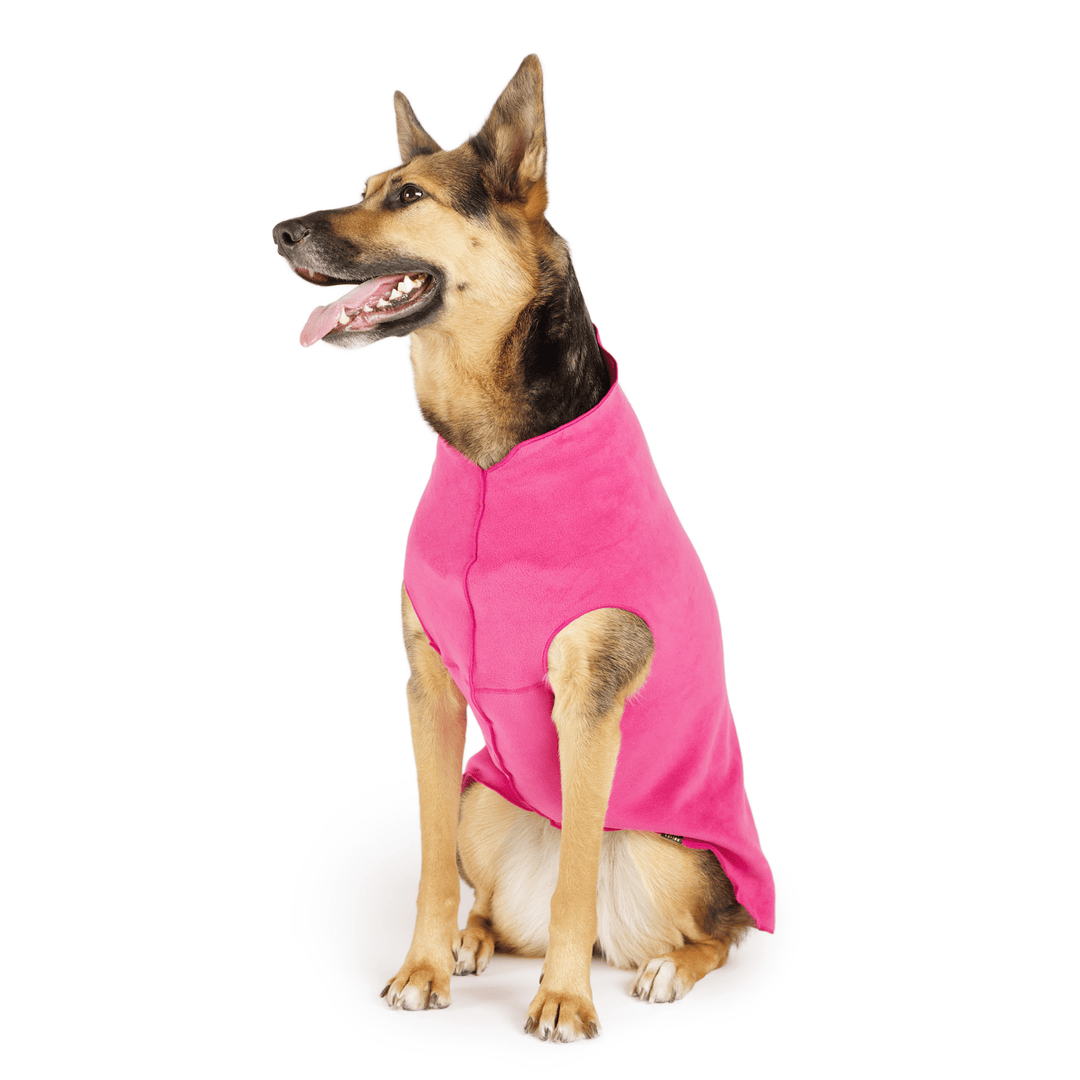 A German Shepherd sits wearing a fuchsia stretch fleece in front of a white background