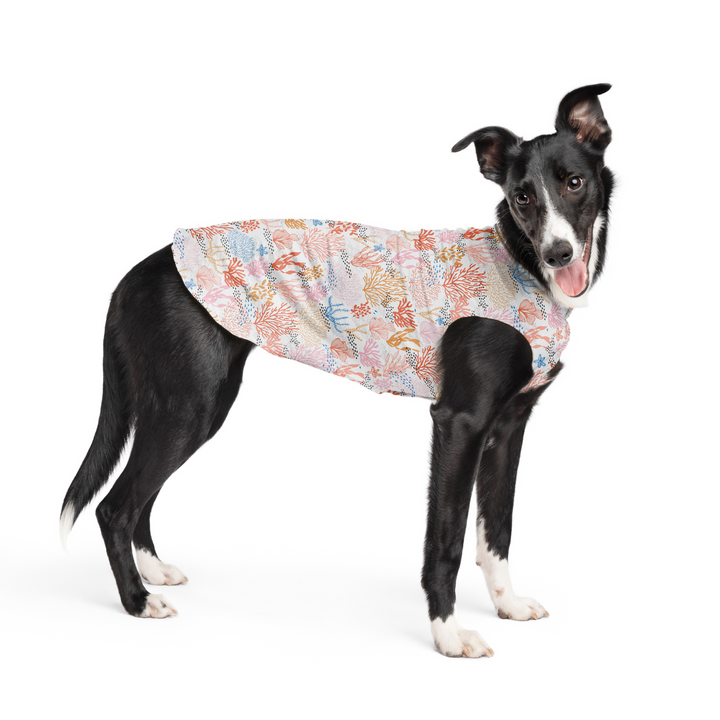 A dog stands wearing a multicolored Coral pattern Sun Tee in front of a white background